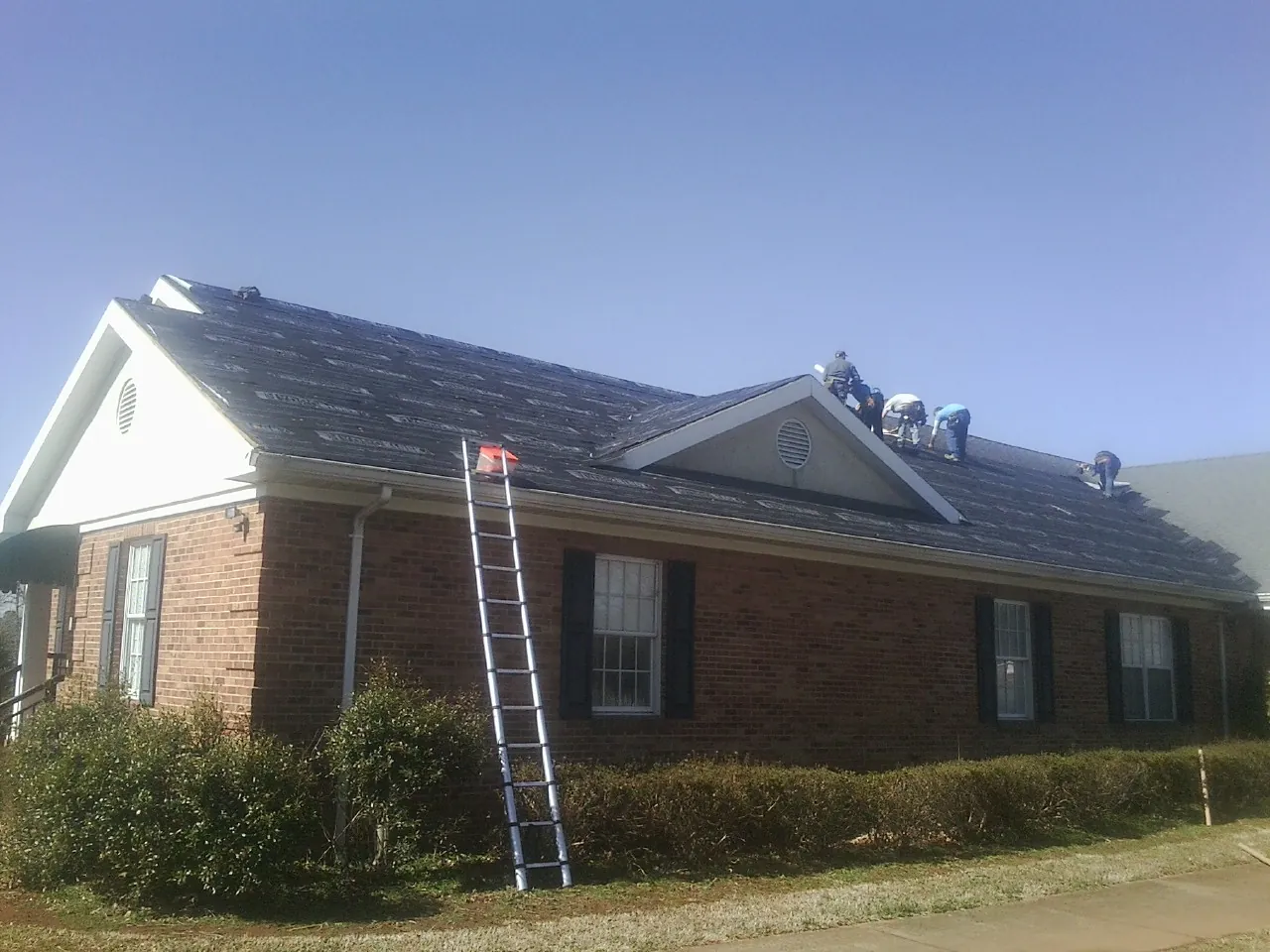 Crew tearing shingles off a brick ranch roof with a ladder set — Metal Roof Repair work by our crew in Central City