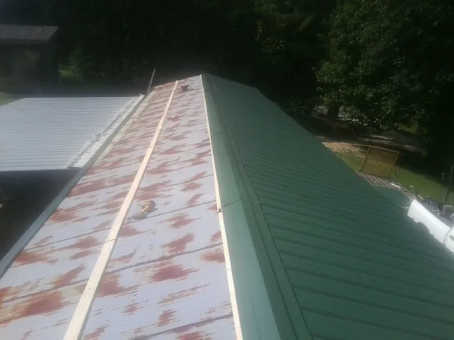 Old rusted panels beside newly installed green metal roofing — Wind Damage Roof Repair by Roofing Brothers in Central City