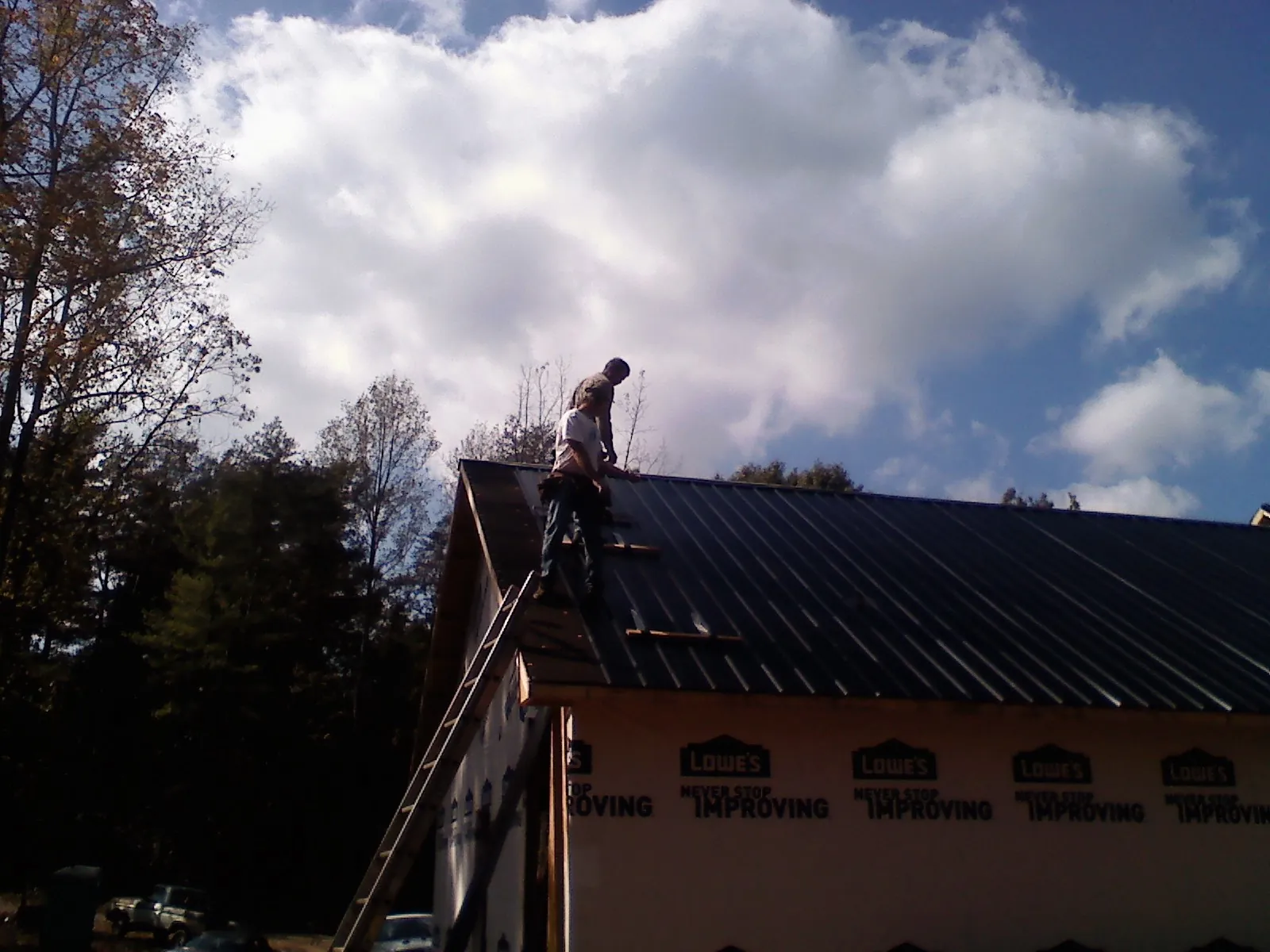Roofer fastening dark metal panels high against a cloudy sky, from a Roof Inspection job in Central City